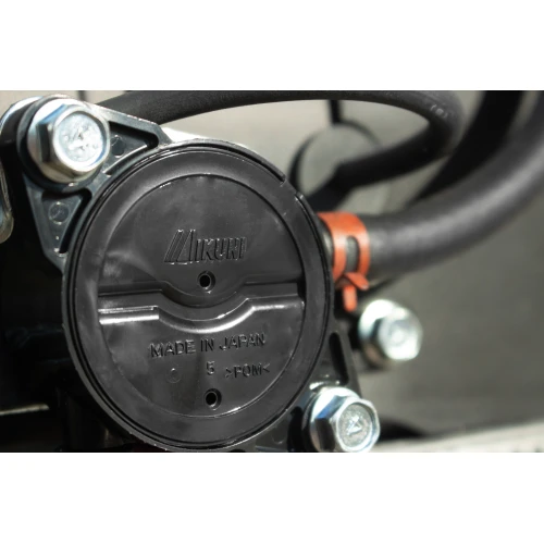 Zbliżenie na czarną, okrągłą część agregatu prądotwórczego z widocznymi śrubami i napisem "Made in Japan". W tle widać fragmenty przewodów i metalowych elementów urządzenia.