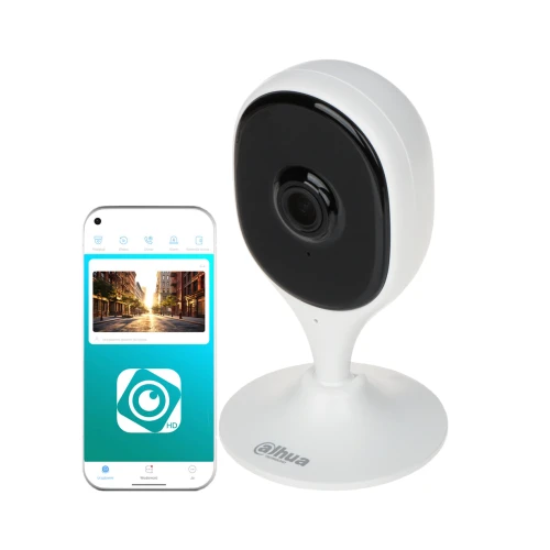 Biała kamera IP o nowoczesnym designie stoi na okrągłej podstawie, obok niej znajduje się smartfon z aplikacją do monitoringu. Na ekranie telefonu widoczny jest interfejs aplikacji z podglądem obrazu z kamery.