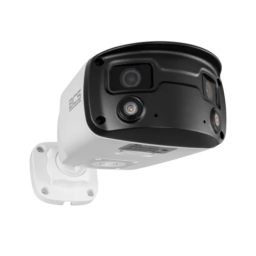 Zdjęcie przedstawia białą, tubową kamerę IP z czarnymi elementami, zamontowaną na białym uchwycie ściennym. Kamera posiada dwa obiektywy i jest oznaczona logo BCS.
