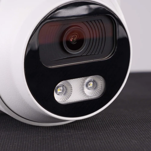 Zbliżenie na białą, kopułową kamerę IP z widocznym obiektywem i dwoma diodami LED na czarnym tle. Kamera leży na ciemnej powierzchni, co podkreśla jej nowoczesny design.