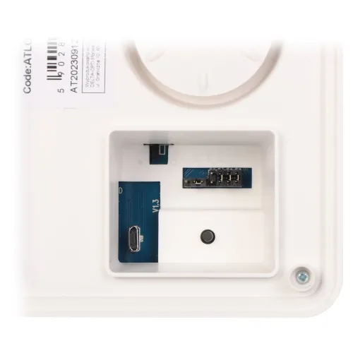 Zdjęcie przedstawia zbliżenie na wnętrze białego urządzenia elektronicznego z widocznym złączem USB i kilkoma pinami. W lewym górnym rogu znajduje się naklejka z kodem i numerem seryjnym.